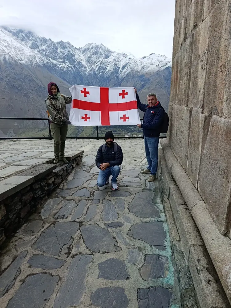 Travellers with the Georgian flag by the walls of Gergeti Trinity Church in Kazbegi